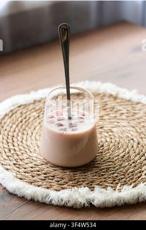 Café Bumble au jus de cerise glacé dans un verre transparent sur une table en bois. Boisson estivale rafraîchissante servie sur un tissu tissé naturel Banque D'Images