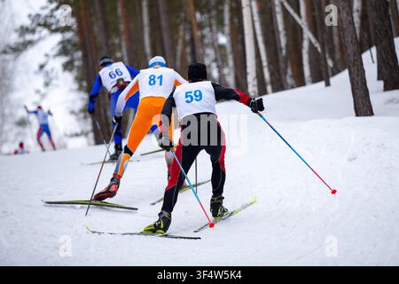 Vue arrière trois athlètes skieurs skate skiant en montée Banque D'Images