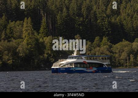 Une scène tranquille d'un petit bateau à moteur touristique naviguant sur un loch serein le long du canal de Calédonie historique dans les Highlands écossais. Journée calme et ensoleillée Banque D'Images