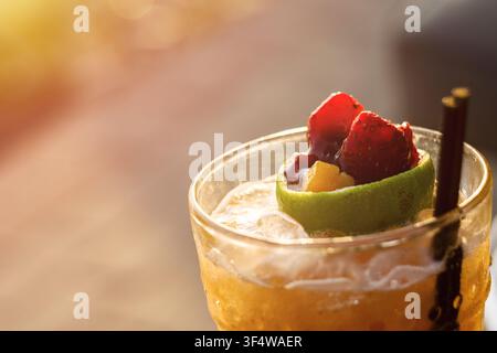 gros plan d'un verre haut rempli d'une boisson glacée de couleur dorée et d'une garniture de fruits frais comprenant des fraises rouge vif et une tranche de citron vert Banque D'Images