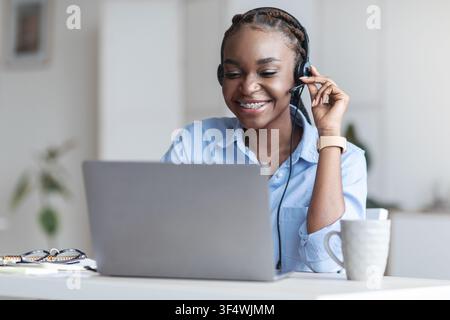 Assistance clientèle. Une femme de direction noire porte un casque et utilise un ordinateur portable au bureau Banque D'Images