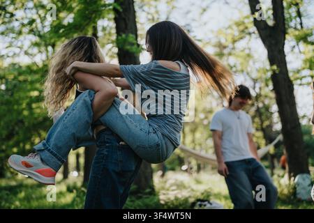 Des amis adolescents se soulevant joyeusement l'un l'autre en passant du temps dans un parc ensoleillé avec des arbres Banque D'Images