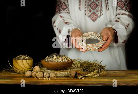 Préserver les traditions séculaires. Scène de repas rituel slave traditionnel kutia avec chemise brodée, bol en bois, bougies, noix et grains sur fond sombre Banque D'Images