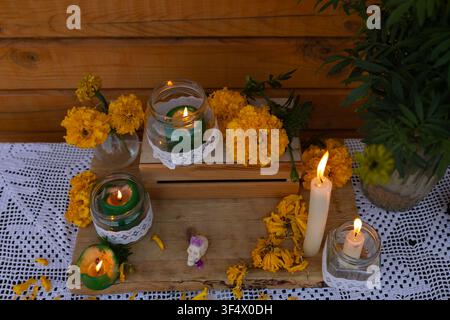 Vue rapprochée d'un arrangement d'autel en soucis avec des fleurs orange vives, des bougies vertes allumées dans des bocaux Mason enveloppés de dentelle, présentoir en caisse en bois, tissu au crochet et décor ambiant chaud et élevé Banque D'Images