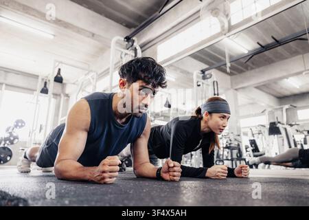 Entraînement en salle de sport : Pose en planche, un homme et une femme effectuent l'exercice de planche dans une salle de sport, concentrés et intenses. Banque D'Images