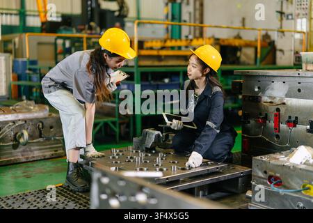 Équipe d'ingénieurs composée de travailleuses acharnées dans une usine d'industrie lourde, jeune ingénieure en formation avec un superviseur adulte Banque D'Images