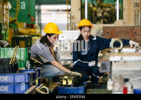 Équipe d'ingénieurs composée de travailleuses acharnées dans une usine d'industrie lourde, jeune ingénieure en formation avec un superviseur adulte Banque D'Images