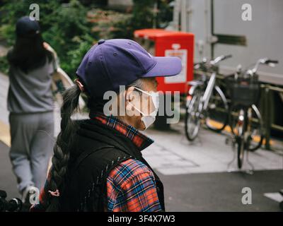 Ancienne femme portant un masque facial et une casquette de baseball marchant dans une rue résidentielle à Shibuya, Tokyo Banque D'Images