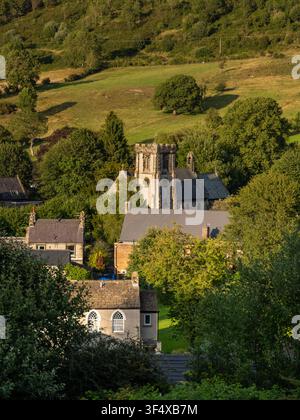 Une vue panoramique élevée capture l'église Saint-Barnabas nichée parmi des arbres verts et des maisons dans la vallée rurale de Bradwell, dans le Peak District, en Angleterre Banque D'Images