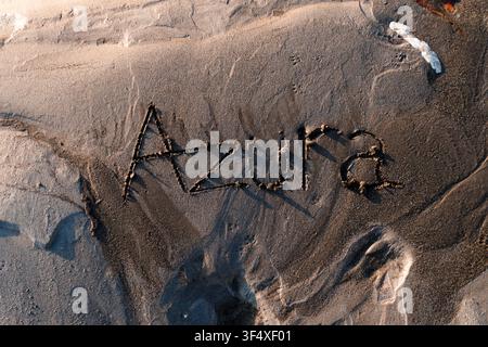 Vue de dessus du nom féminin « Azura » écrit à la main dans le sable humide de la plage pendant la lumière chaude de l'heure dorée. Banque D'Images