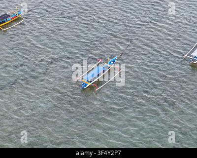 Vue aérienne de bateaux à balancier traditionnels jukung flottant sur les eaux claires et peu profondes de Mertasari Beach à Denpasar Selatan, Bali, Indonésie. Banque D'Images