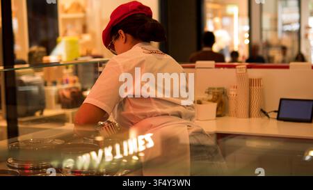 Serveur de crèmerie servant du gelato – Comptoir de gelaterie artisanale avec bacs en acier inoxydable, travailleur des services alimentaires Banque D'Images