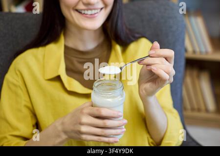 Gros plan d'une femme mangeant du yaourt avec une cuillère à la maison, concept de collation saine Banque D'Images
