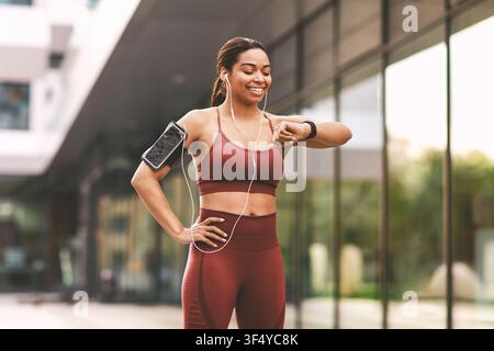 Jeune femme noire heureuse vérifiant sa montre connectée en courant en plein air, concept de fitness Banque D'Images