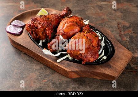 Poulet Tandoori servi sur un plat en fonte grésillant avec du chou, de l'oignon rouge et une tranche de citron vert sur une planche de service en bois. Grillé indien traditionnel c Banque D'Images