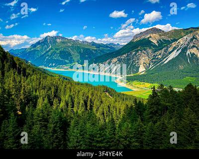 Vue panoramique du lac turquoise de Resia (Reschensee) entouré de majestueux monts alpins et de forêts vertes denses dans le Sud-Tyrol, en Italie Banque D'Images