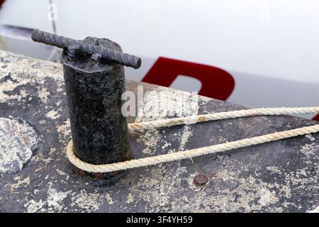 Poteau d'amarrage en fer rouillé sur un quai en béton patiné, tenant solidement une corde blanche, offrant un détail en gros plan d'équipement nautique et de sa maritime Banque D'Images