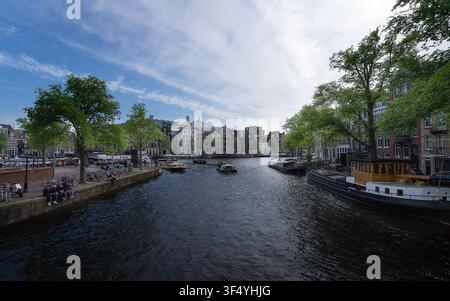Canal traditionnel d'Amsterdam bordé de bâtiments historiques et de bateaux sous un ciel nuageux Banque D'Images