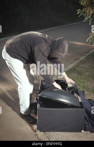 Homme en sweat à capuche noir organisant et préparant du matériel photographique professionnel en extérieur Banque D'Images