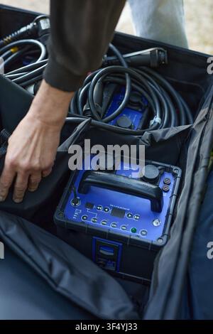 Homme en sweat à capuche noir organisant et préparant du matériel photographique professionnel en extérieur Banque D'Images