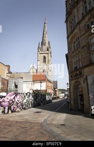 Sheffield, Angleterre, Royaume-Uni - 15 juillet 2026 : Vue de la flèche de l'église cathédrale Sainte-Marie s'élevant au-dessus d'une rue avec un mur recouvert de graffitis Banque D'Images