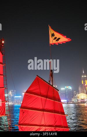 Gros plan vertical d'une voile de jonque rouge traditionnelle et d'une bannière flottante la nuit avec le ciel illuminé de Victoria Harbour, Hong Kong. Banque D'Images