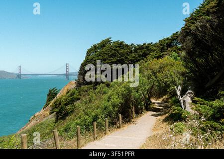 Un sentier de randonnée pittoresque serpente le long des falaises côtières près de San Francisco, offrant des vues panoramiques sur le Golden Gate Bridge au loin. Banque D'Images