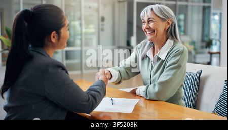 Sourire, vieille femme et poignée de main à la maison avec un conseiller, transaction immobilière et contrat d'achat. Personne âgée, serrant la main et merci pour Banque D'Images