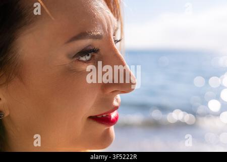 Profil de plage d'une femme vue de côté, une belle femme d'âge moyen regardant l'océan bleu étincelant avec espace de copie Banque D'Images