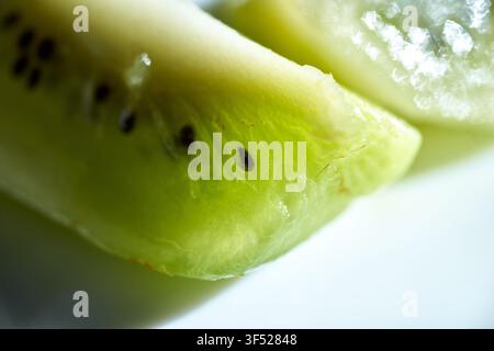 Grossissement macro des tranches de kiwi vert frais mettant en valeur la pulpe juteuse vibrante et les minuscules graines noires en lumière douce et translucide délicate Banque D'Images