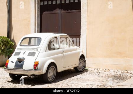 Fiat 500 blanc vintage garé dans une cour pavée de bâtiments en pierre jaune pâle en Sicile Banque D'Images