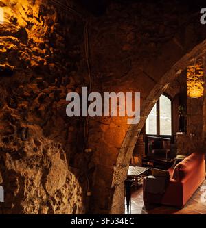 Intérieur méditerranéen douillet avec des murs en pierre rustique, des poutres en bois, des meubles vintage et une vue sur les montagnes à travers de grandes fenêtres en arc. Ambiance chaleureuse Banque D'Images