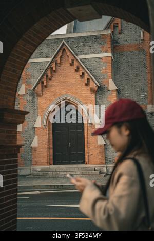 Femme vérifiant son téléphone sous une arche en briques près de l'Union Church, Shanghai Banque D'Images