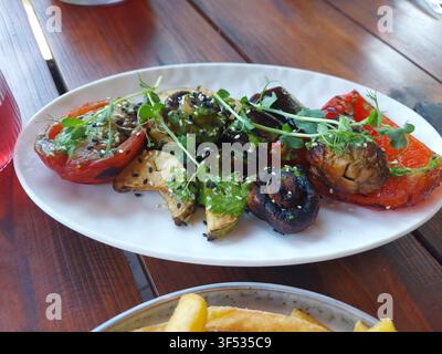 Légumes grillés avec pesto et graines de sésame disposés sur une assiette, sur une table de repas en plein air, avec poivrons rouges grillés, champignons, sauce pesto, graines de sésame, vue de dessus. Banque D'Images