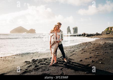 Jeun couple heureux s'embrassant sur une plage de sable noir Banque D'Images