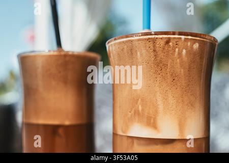 Vue rapprochée de deux verres hauts remplis de café glacé grec traditionnel en frappe, surmontés d'une mousse riche et servis avec des pailles en plastique colorées sur un Banque D'Images