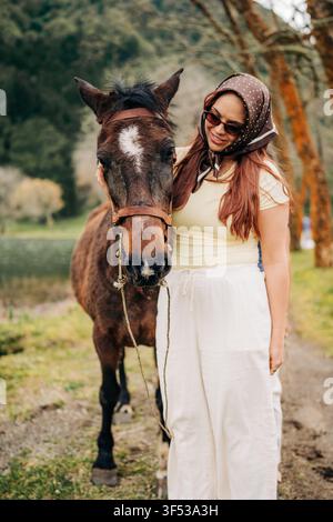 Femme élégante avec foulard caressant un cheval brun Banque D'Images