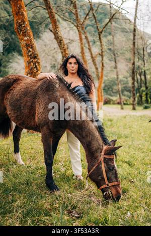 Jeune femme debout avec un cheval en train de brouter dans un champ Banque D'Images