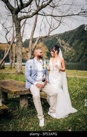 Couple de jeunes mariés célébrant avec du champagne en plein air Banque D'Images