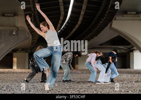 Jeune femme en jean ample dirige une équipe de danse urbaine Banque D'Images