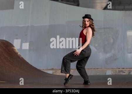 Femme confiante portant un fedora dansant dans un skatepark Banque D'Images