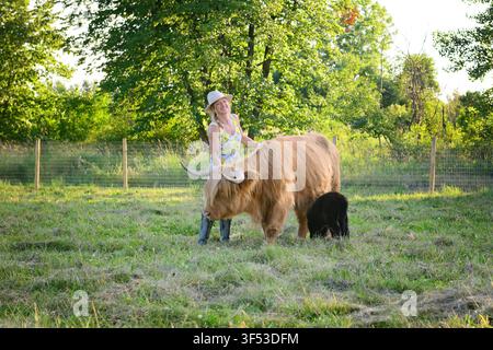 Femme heureuse caressant une vache des Highlands et son veau pelucheux Banque D'Images