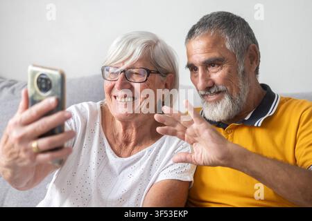 Couple de seniors heureux faisant un signe de la main lors d'un appel vidéo à la maison Banque D'Images