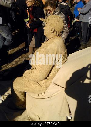 Un artiste de rue est assis sur un banc imitant une statue en argile lors d'une performance devant les touristes attentifs sur une rue typique de Madrid, en Espagne. Banque D'Images