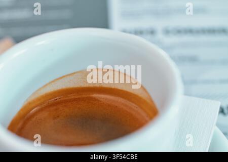 Gros plan d'une petite tasse en céramique blanche remplie d'un café espresso fraîchement préparé montrant une crème brune riche au sommet dans un cadre de café avec un arrière-plan flou Banque D'Images