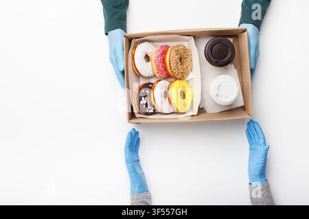 Le client qui porte des gants en caoutchouc récupère la commande. Le garçon donne une boîte avec des beignets avec glaçure et deux tasses de café, à emporter Banque D'Images