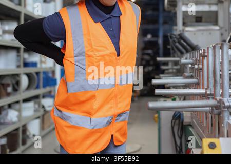 Une femme sur une chaîne de production dans une usine manufacturière ressent des douleurs au bas du dos pendant le travail. Banque D'Images