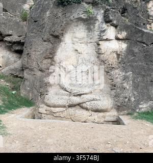 Vue de la gravure rupestre antique de Bouddha de Ghaligai encastrée dans une paroi rocheuse avec des détails en pierre érodée et un sol herbeux à Ghalegay, Khyber Pakhtunkhwa, Banque D'Images