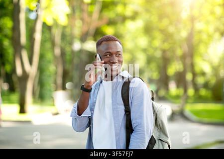 Portrait d'un beau homme afro-américain qui parle à son ami téléphone portable au parc Banque D'Images