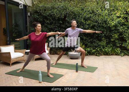 Couple divers pratiquant le yoga debout sur des tapis verts sur une terrasse en chevrons avec des bouteilles d'eau Banque D'Images